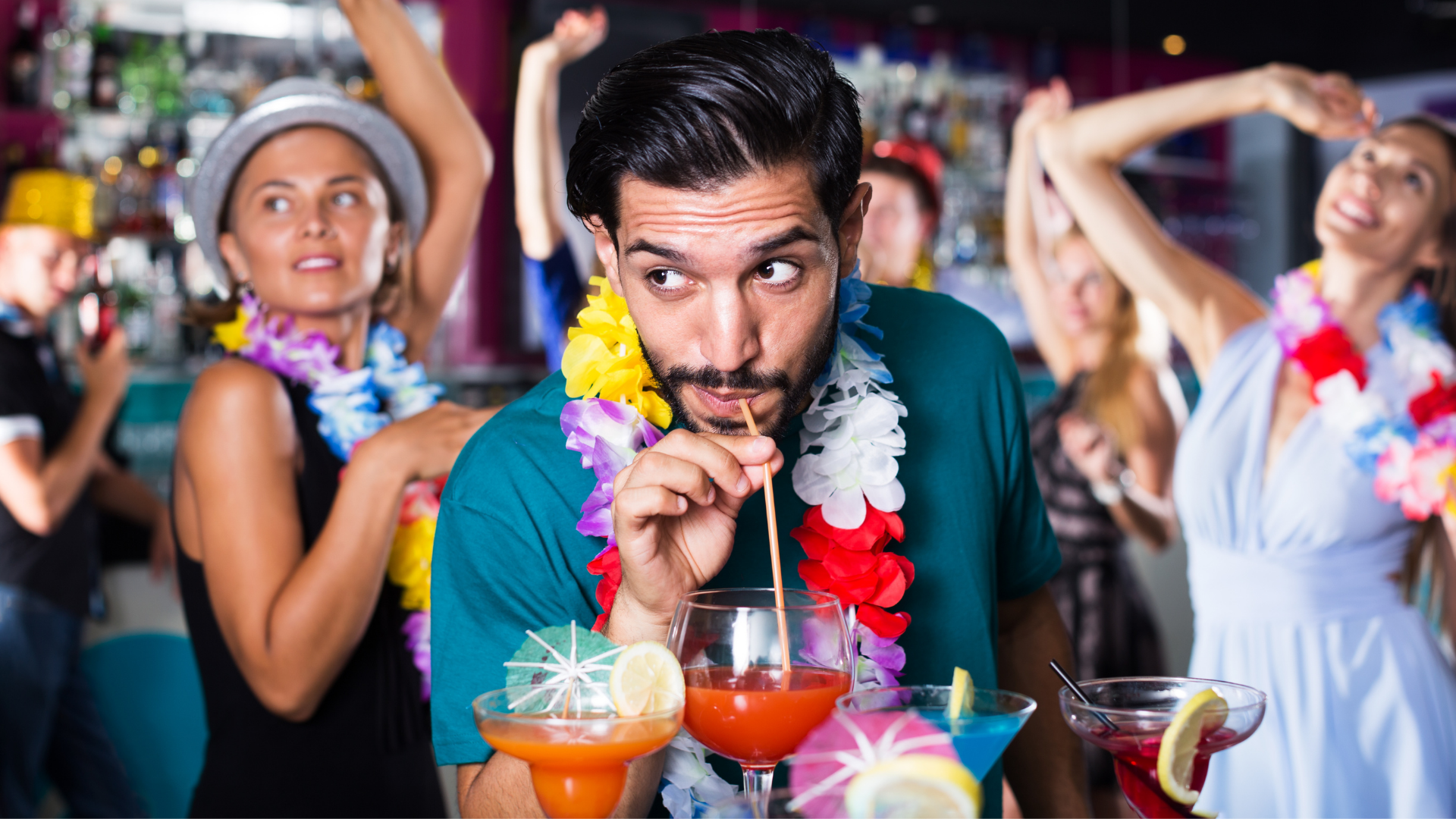 man at party wearing lei sipping on tiki cocktail