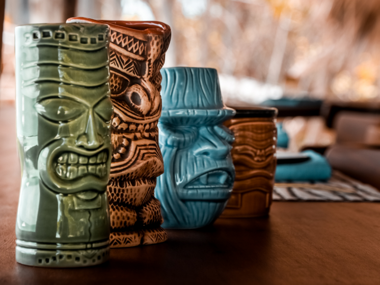 green brown and blue tiki glasses on a bar